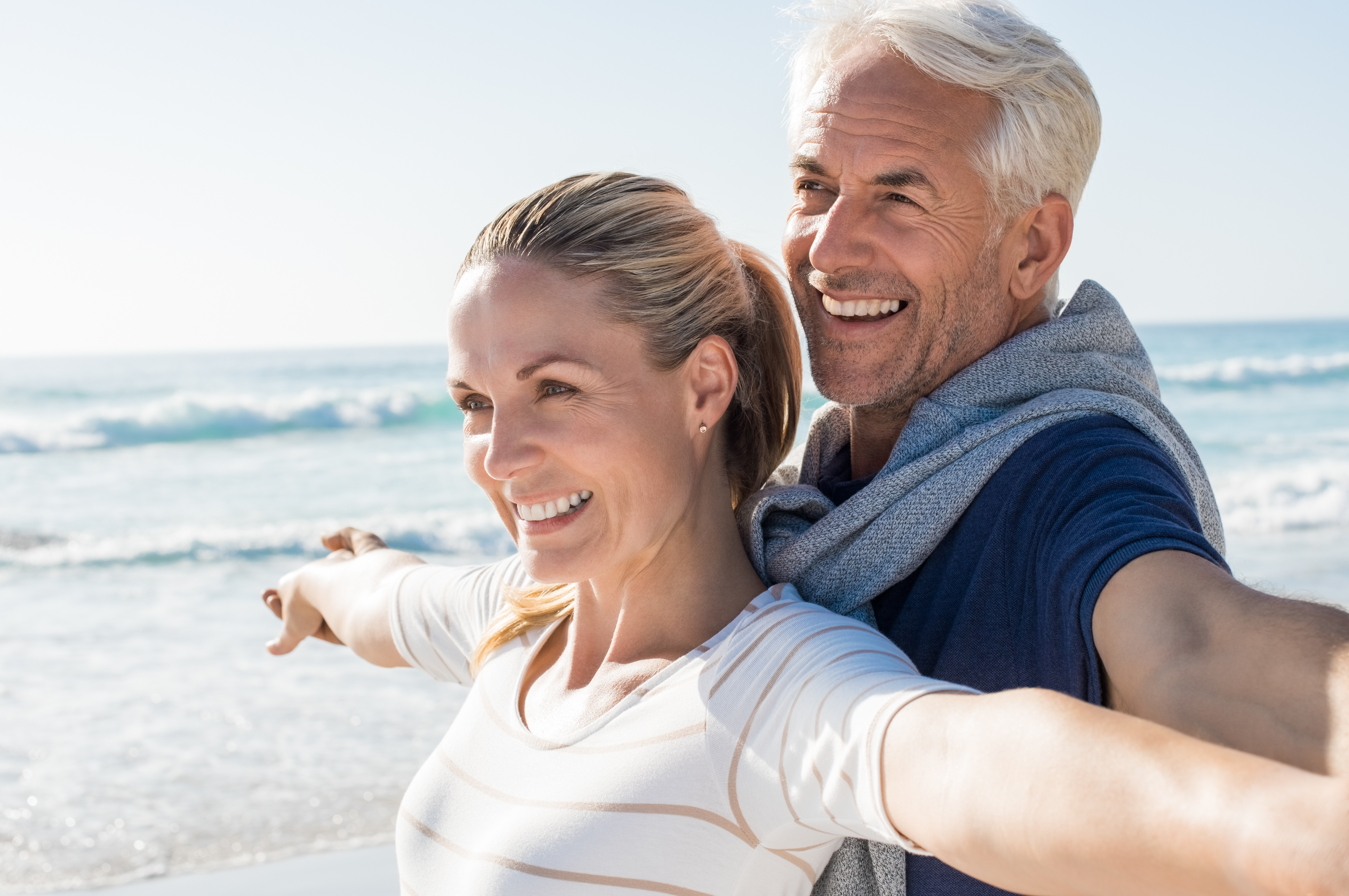 Carefree mature couple Happy senior couple standing on beach with arms outstretched and looking away. Happy couple at beach on a bright sunny day. Retired husband and smiling wife thinking about their future.